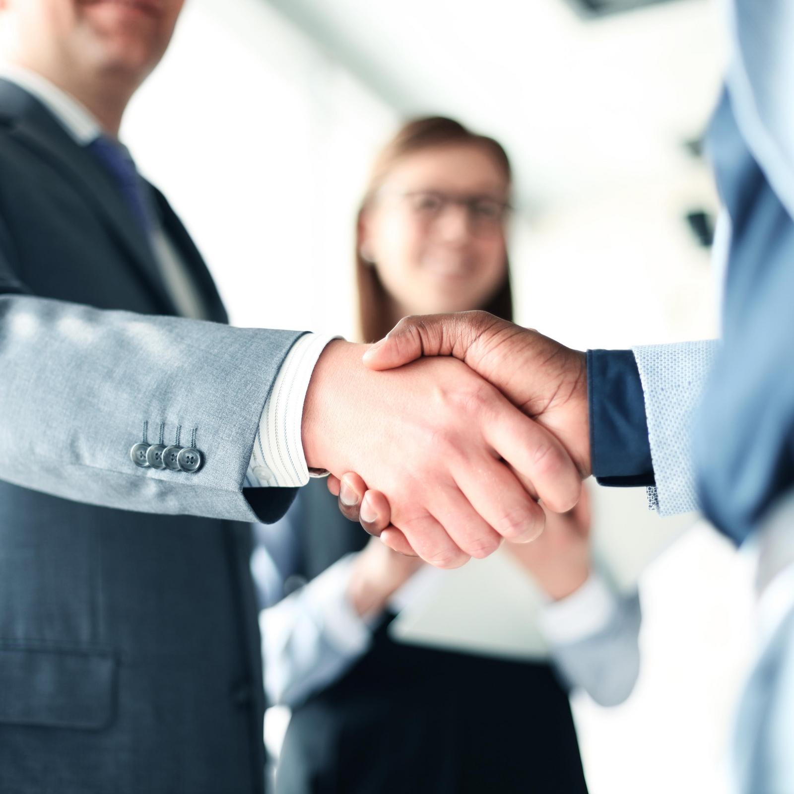 handshake between two businessmen with women in background